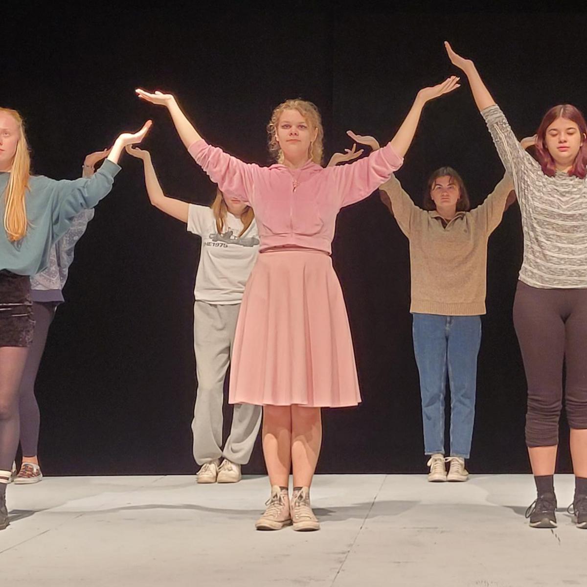Six actors stand in two lines holding their arms up over their heads while rehearsing a scene at Malaspina Theatre.