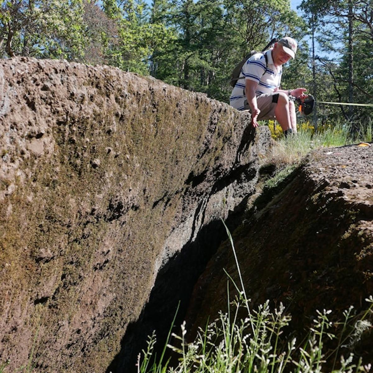 A man sits and observes a large crack in the ground