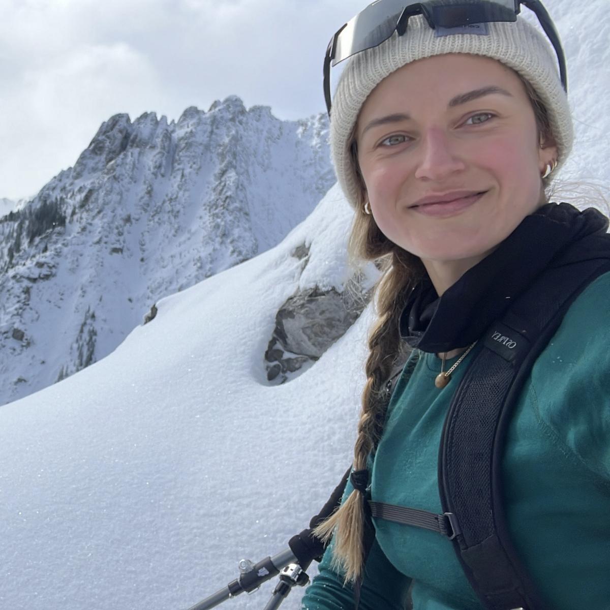 Andrea wearing ski gear smiles with a snowy mountainscape behind her