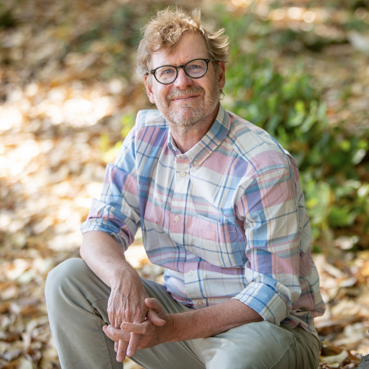 Erik Krogh sitting on the ground outside on a sunny day and smiling at the camera.