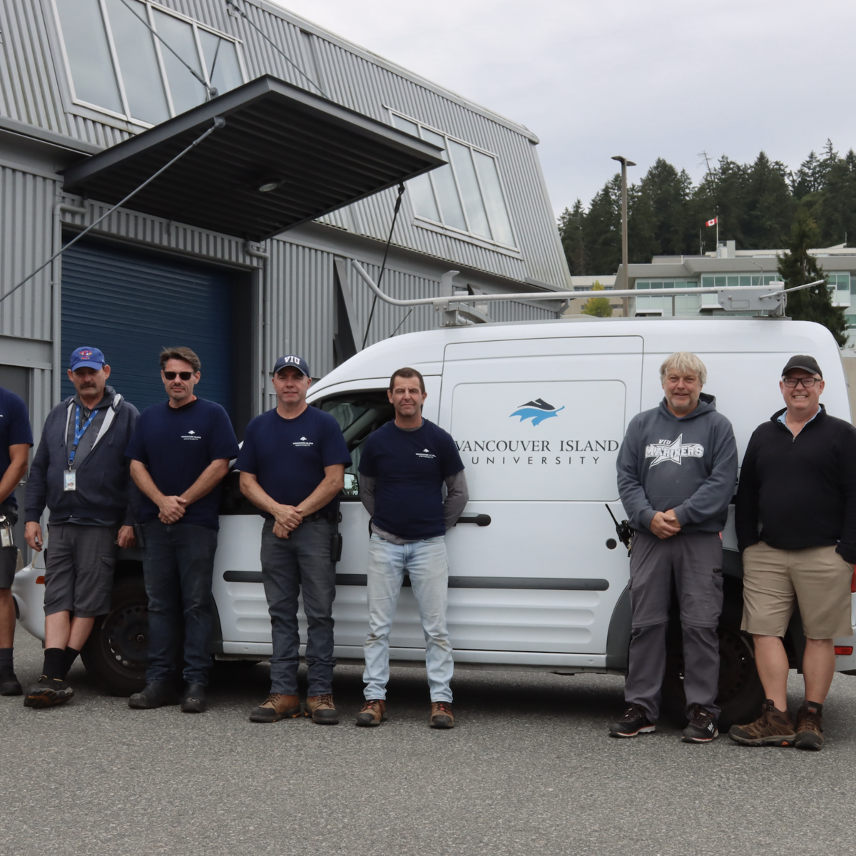 The facilities team at VIU standing outside in front of a work van on a cloudy day