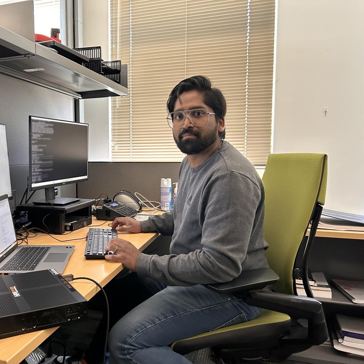 Yadhu Sivan sitting at a computer desk with three monitors and looking at the camera.