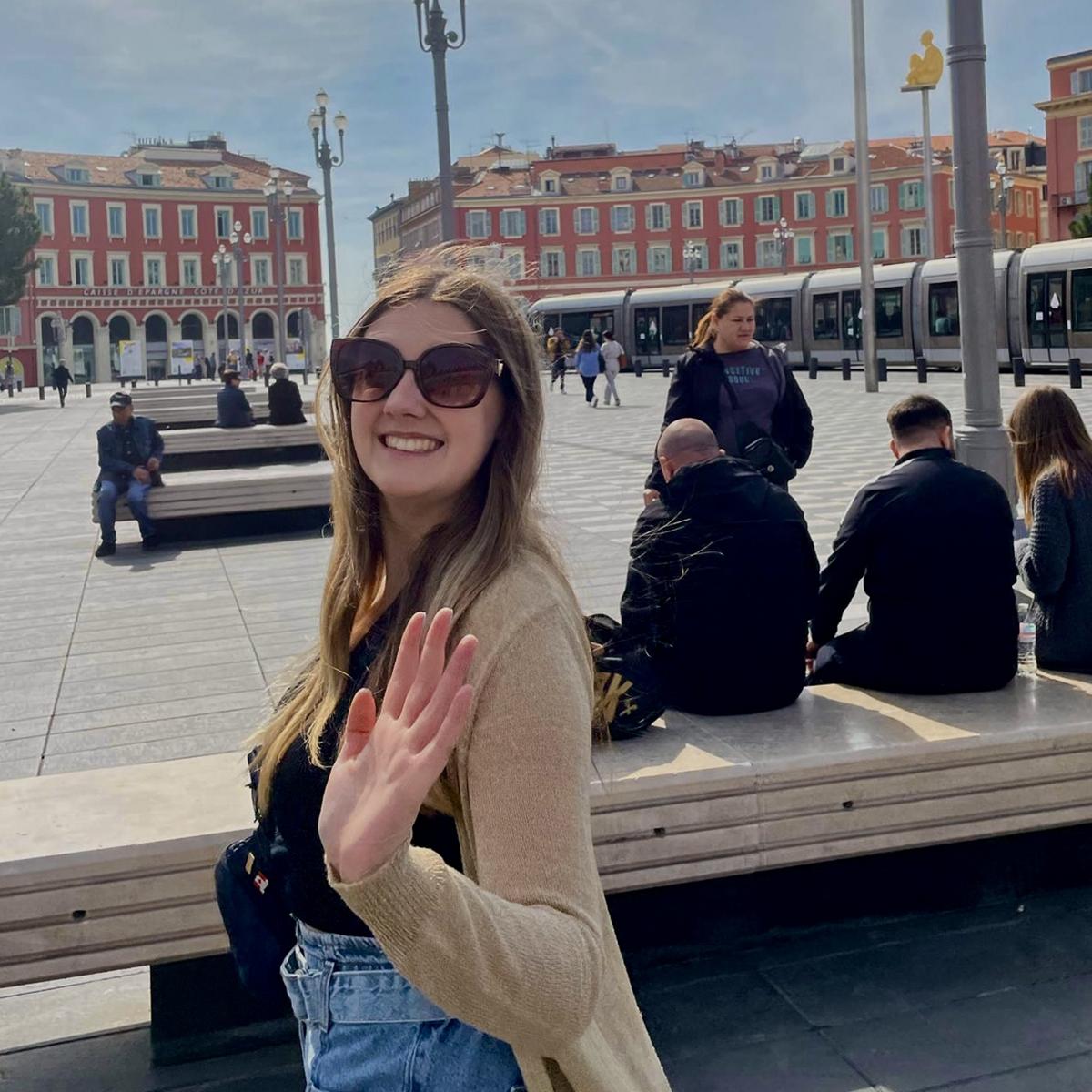 Jenna waves at the camera in a square