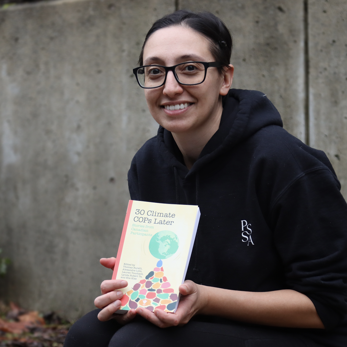 Lauren Touchant sitting outside and displaying her book and smiling at the camera.