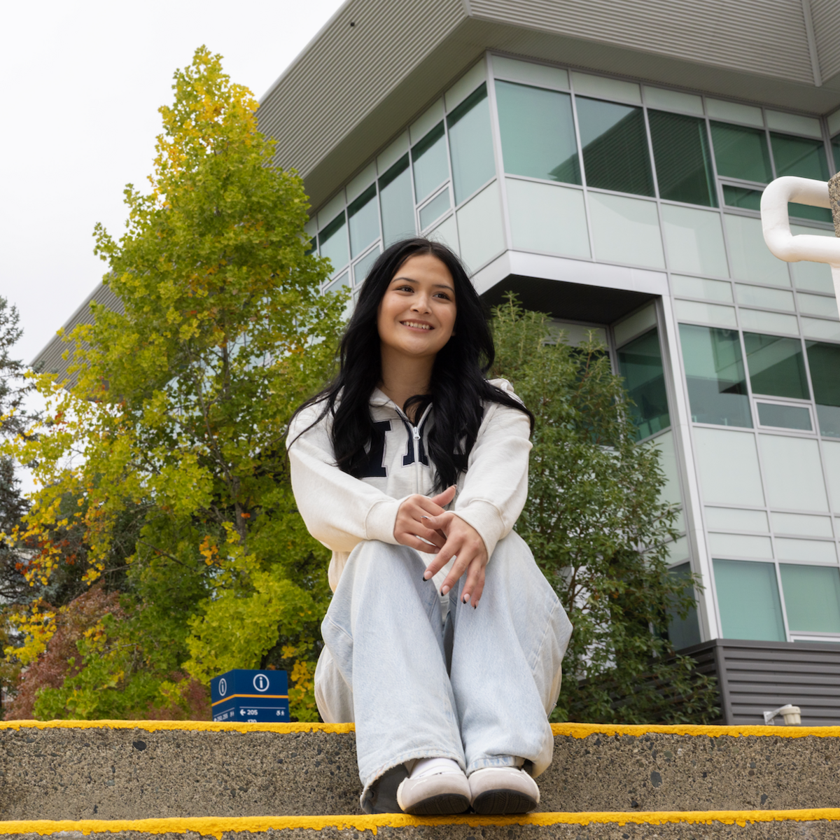 Marissa Tom-Charlie sitting on steps outside on a cloudy day, smiling and looking off into the distance