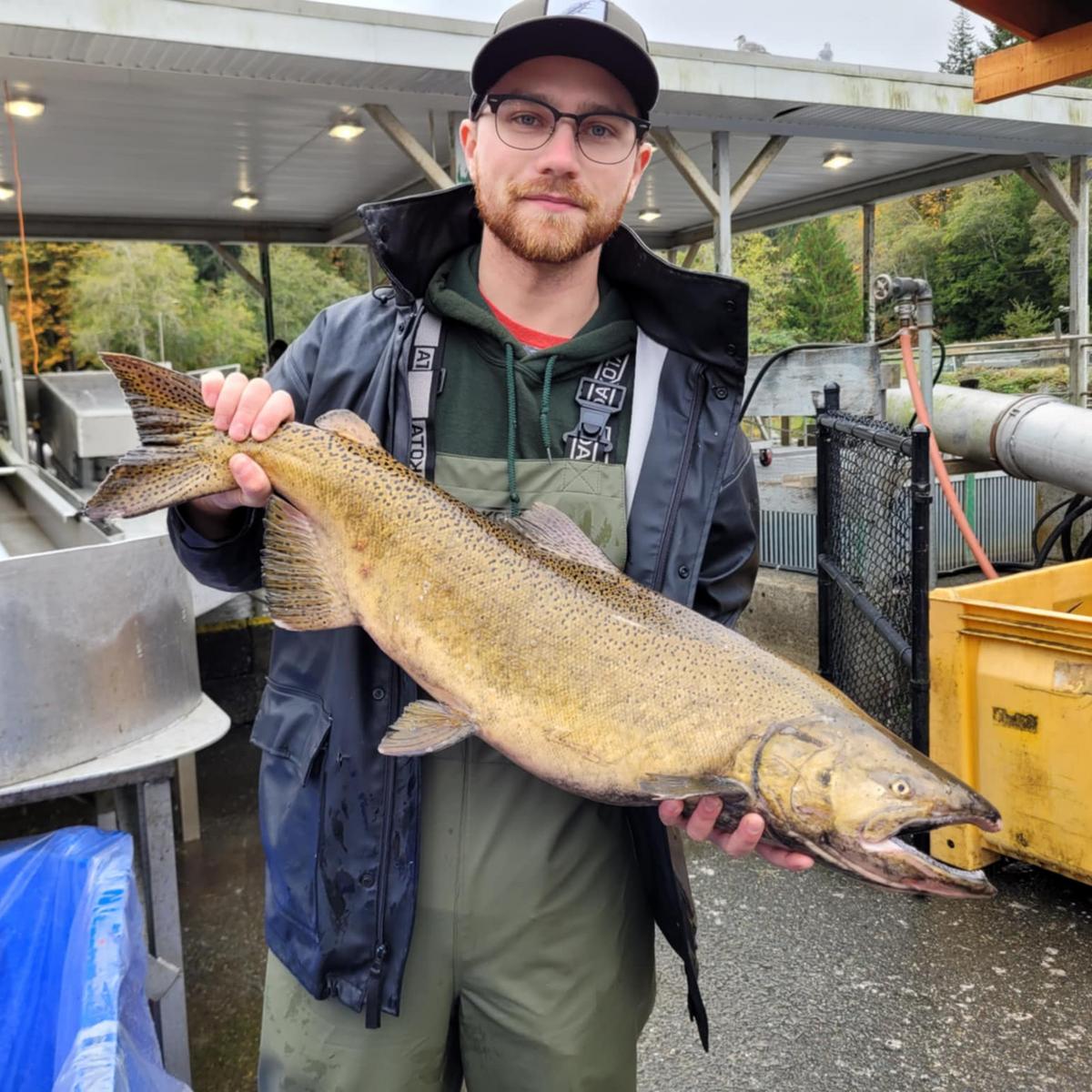 A man wearing hip waders and waterproof jacket holds a salmon