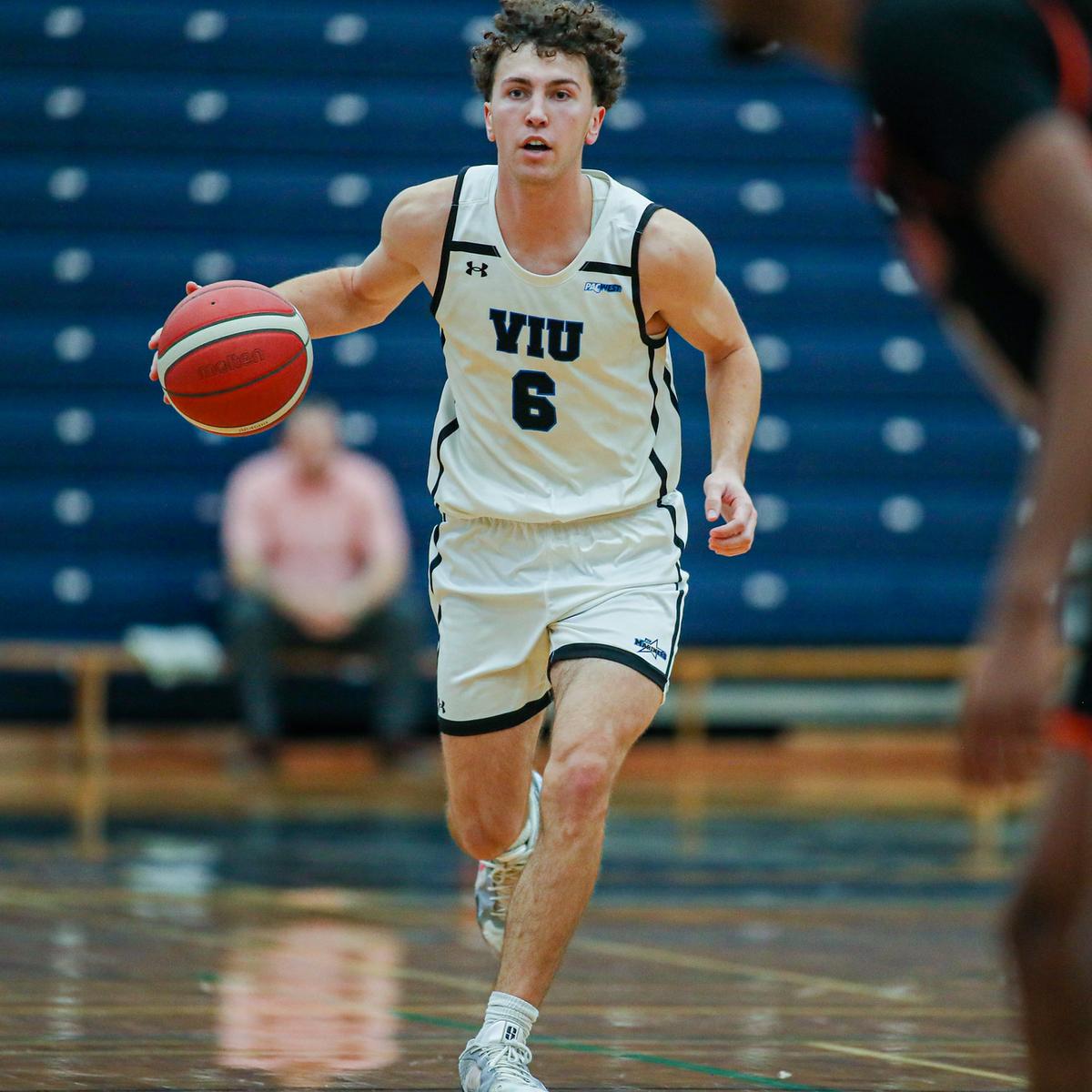 Ryan Bastian wearing a Mariners uniform running with the basketball during a game in a gym.