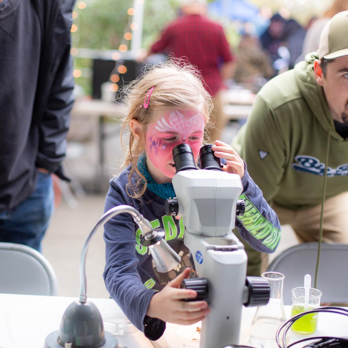 A young girl looking through a microscope during an exhibit at VIU Fest.
