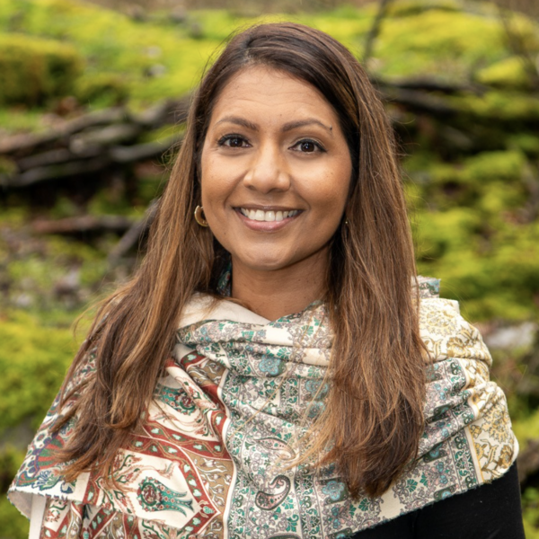 CAroline VAriath standing outside against a green backdrop and smiling at the camera.