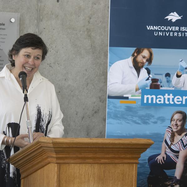 Dr. Deborah Saucier, VIU President and Vice-Chancellor, stands in front of a podium smiling.