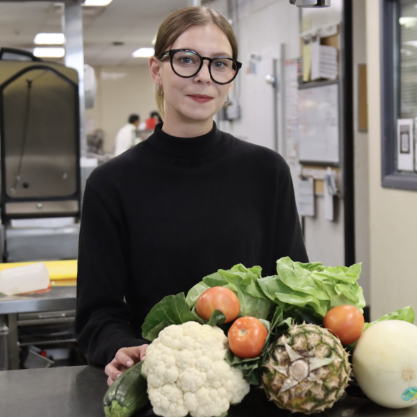 Isabelee standiing at a table in an industrial kitchen with a plate pf fruit and vegetables in front of her