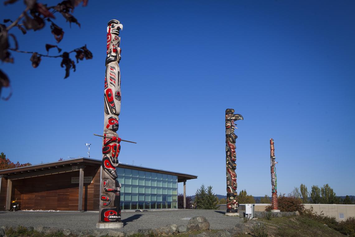 Image of three totem poles in front of Shq'apthut, the Gathering Place on VIU's Nanaimo campus