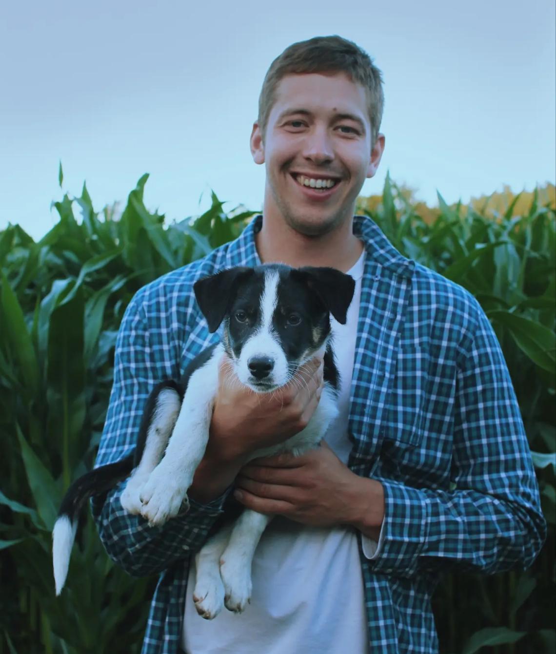 Douglas Groenendijk holds a black and white dog while standing in a field.