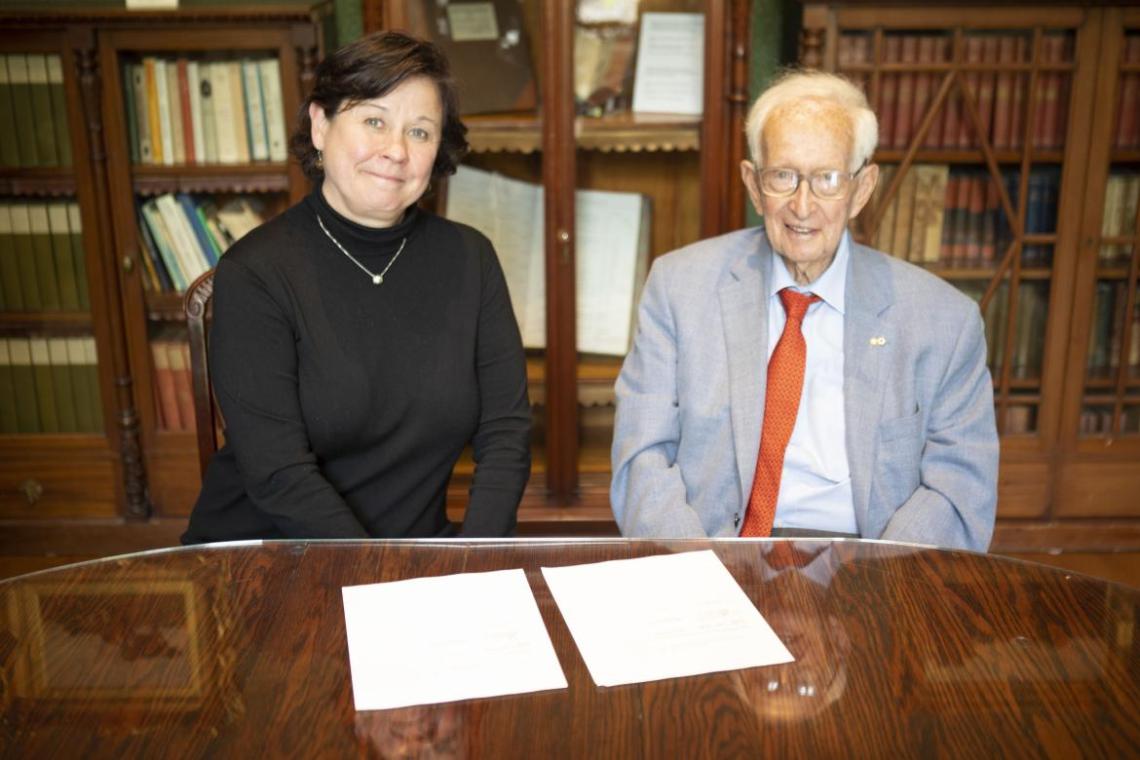 Deborah Saucier and Stephen Jarislowsky signing documents seated at a table