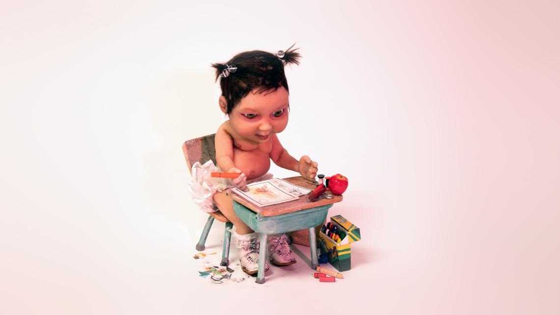 A cartoon baby sits at a school desk with colouring supplies