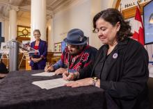 Two people sign papers while a third in the background looks on