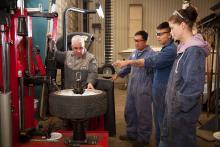 three automotive students receive instruction from a teacher in the shop