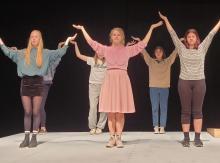 Six actors stand in two lines holding their arms up over their heads while rehearsing a scene at Malaspina Theatre.