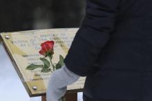 A person holding a rose stands in front of the Jardin des Quartorze garden memorial.