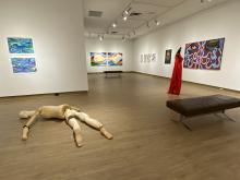Interior of the View Gallery with paintings hung on the wall and a wooden human body art piece on the floor.
