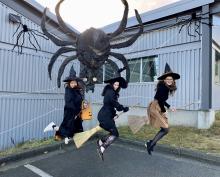 Three women on witches who look like they are flying with a large spider behind them.