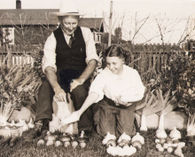 A man and a woman kneel behind produce laid out on grass