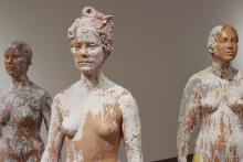 Three sculptures of a person splashed with white paint.