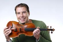James Mark smiles while holding a violin.