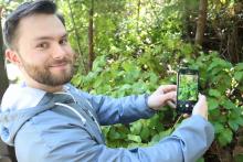Jacob Frankel holds up his phone to a sala bush. The green leaves appear on his phone screen.