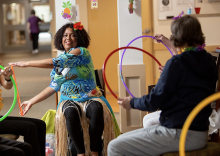 Telma Dos Santos sitting in a chair in front of a group of seniors who are all playing with a Hua hoop in their hands