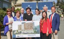 Group photo of people standing with a rendering of the new student housing building