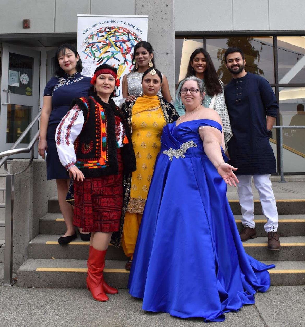 A group of people in various cultural attire standing in front of a WorldVIU sign on the steps of the VIU library