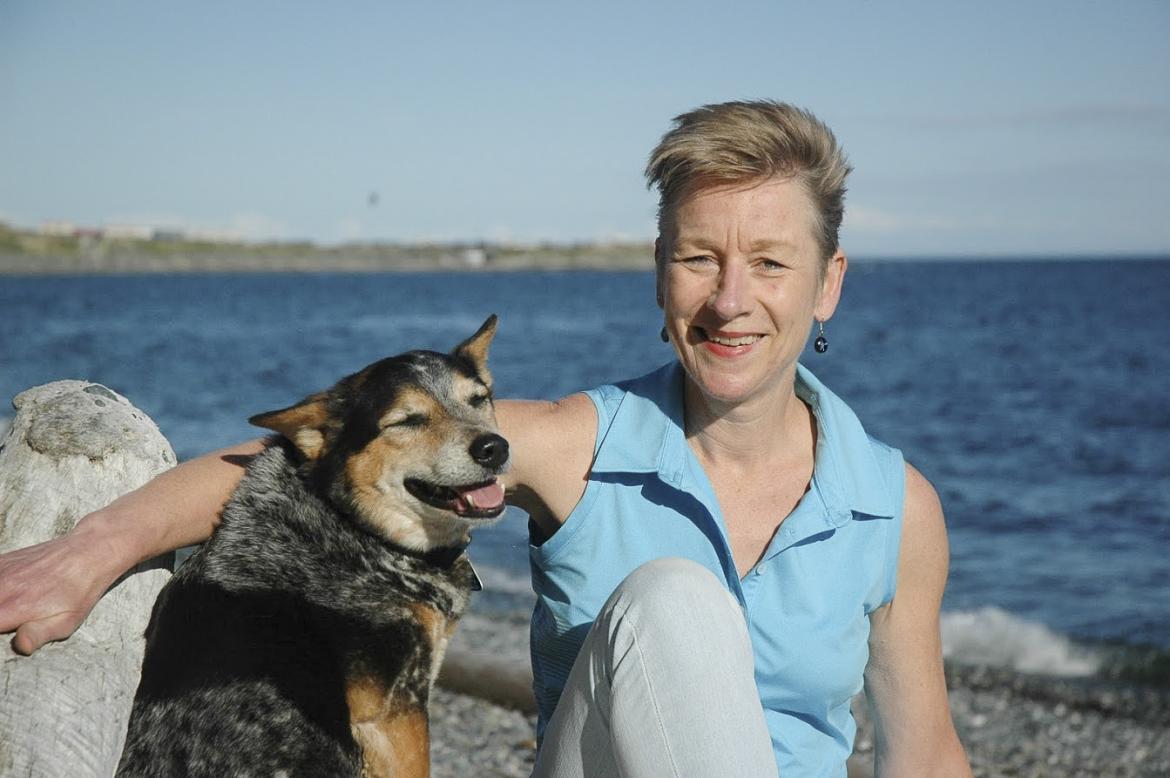 Debra Hellbach sits on the beach with a dog.