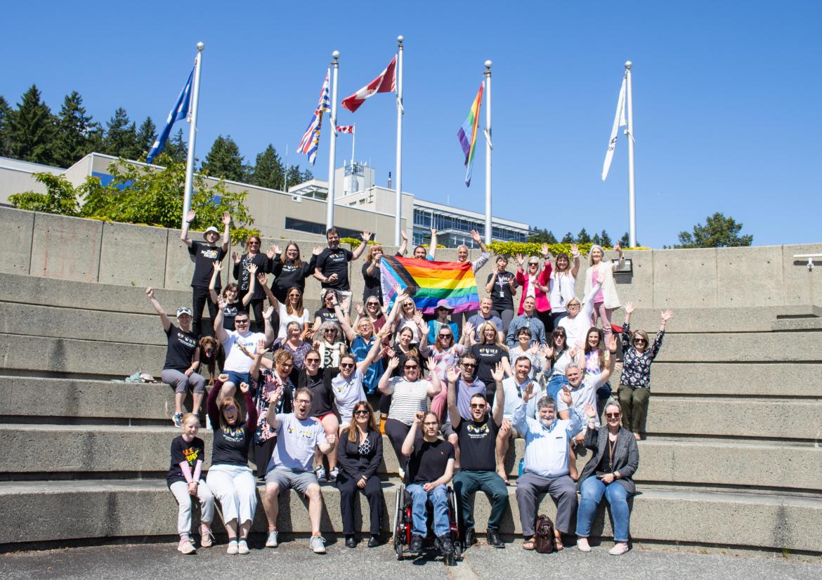 A group wearing Pride t-shirts poses for a photo with the pride flag