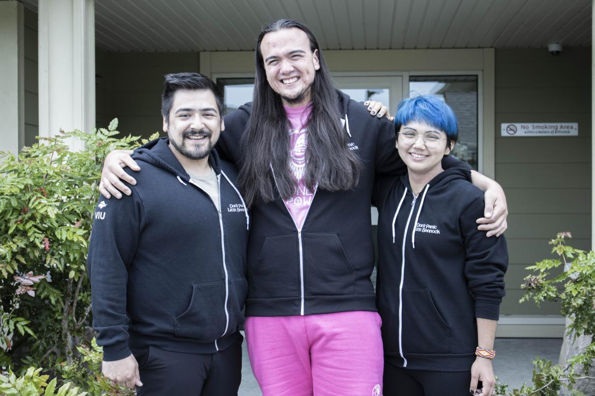 Three people standing in front of a VIU residence building