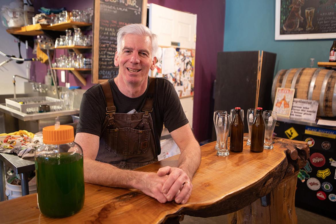 Dave Paul, owner of Love Shack Libations, leans against a wooden counter. Beer bottles and a glass is on his right.