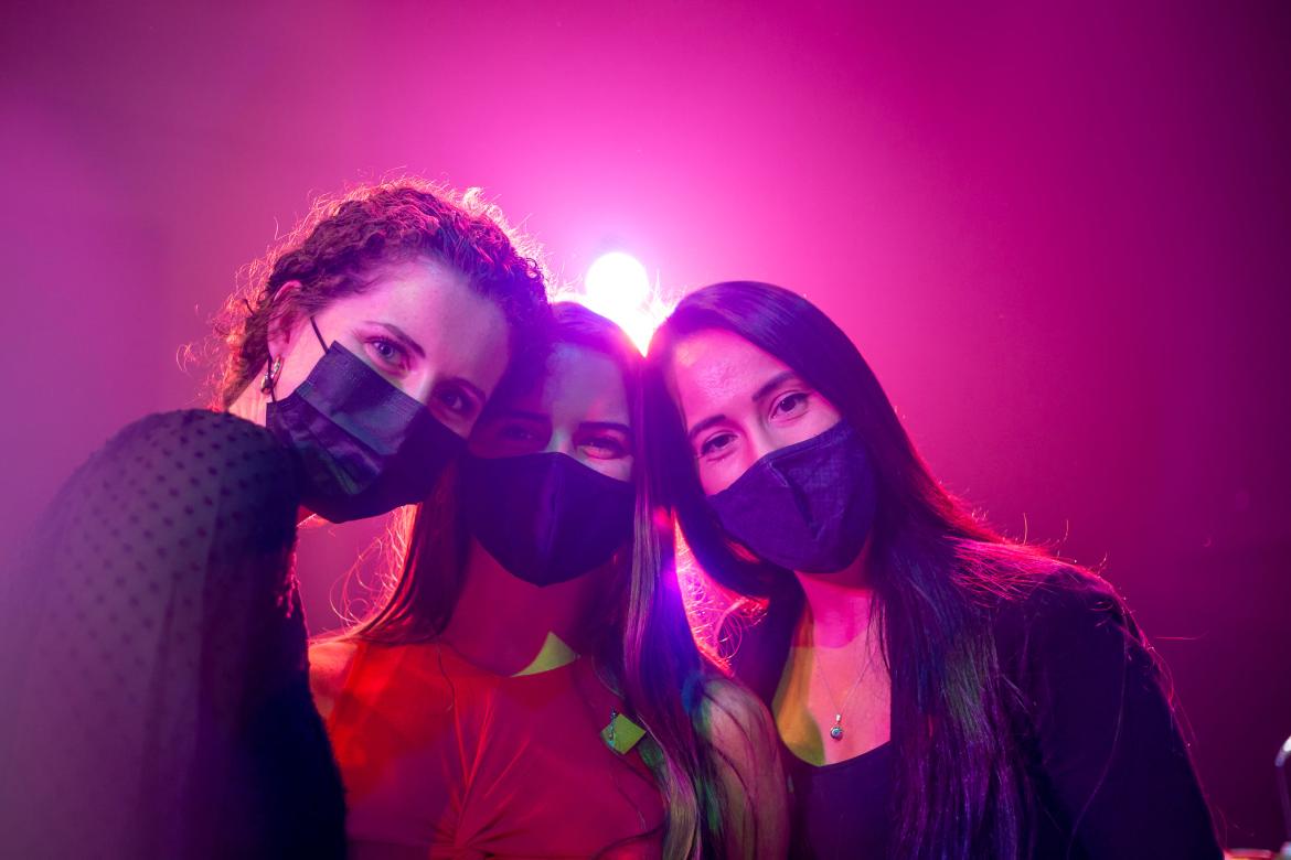 Three women posing in masks with a stage light behind them