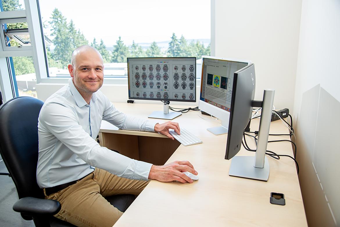 Sandy sits at his desk with images of brains open on one screen