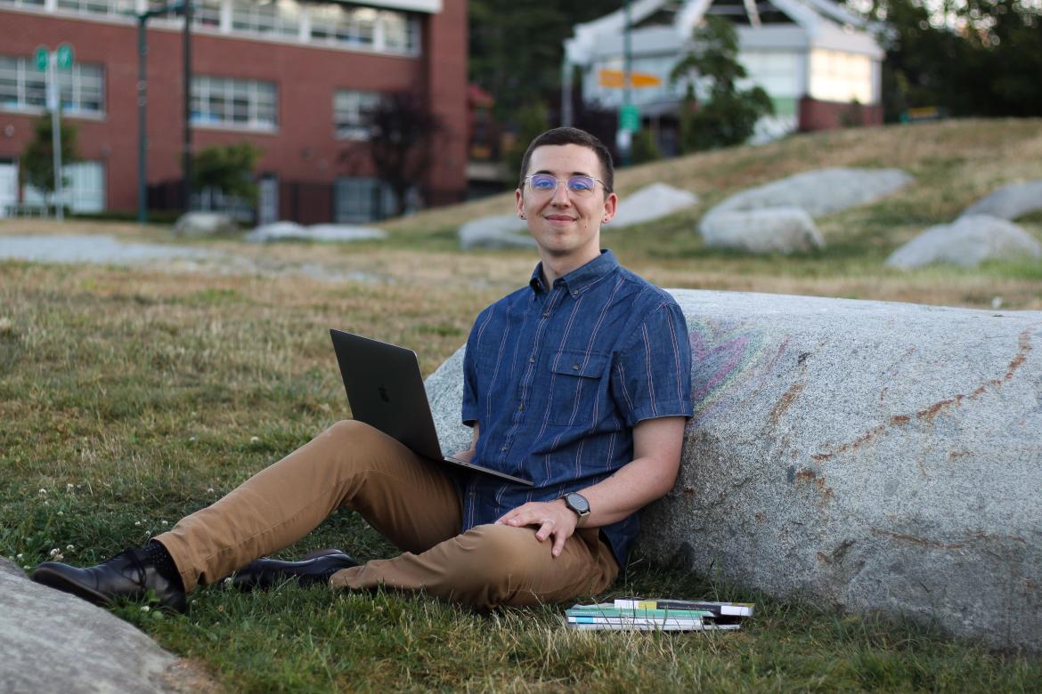 Spenser Smith, a VIU Creative Writing alum, seated outdoors with his laptop
