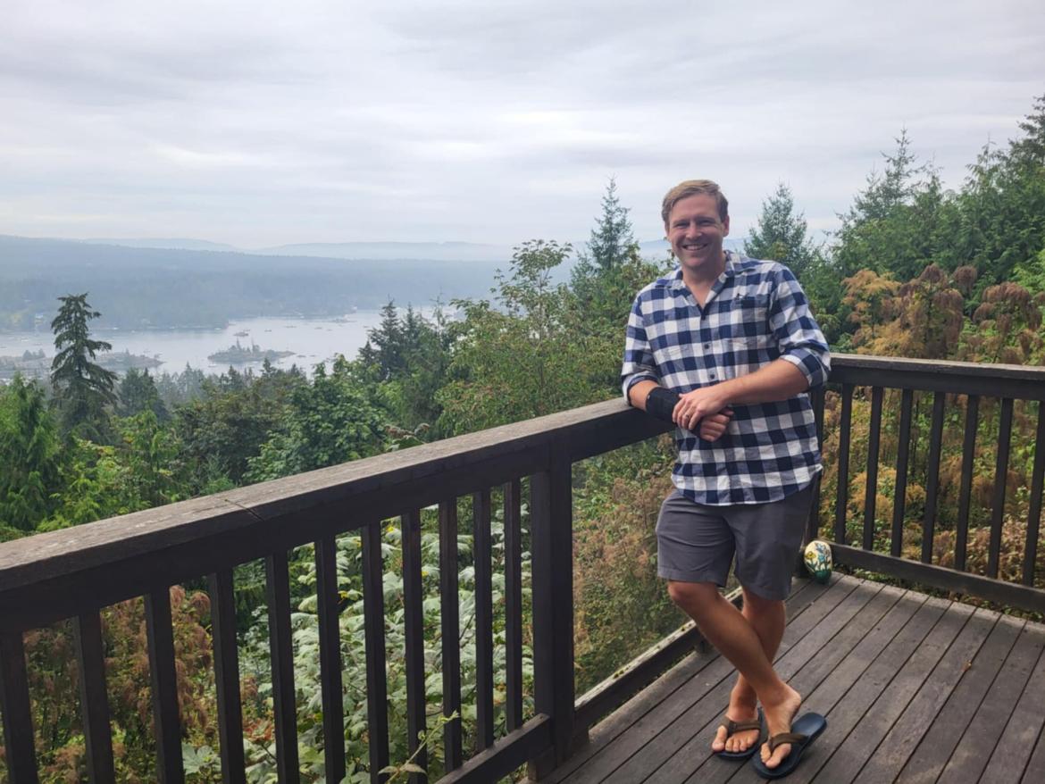 Stephen Hextall leans against a railing with trees and a lake in the background.