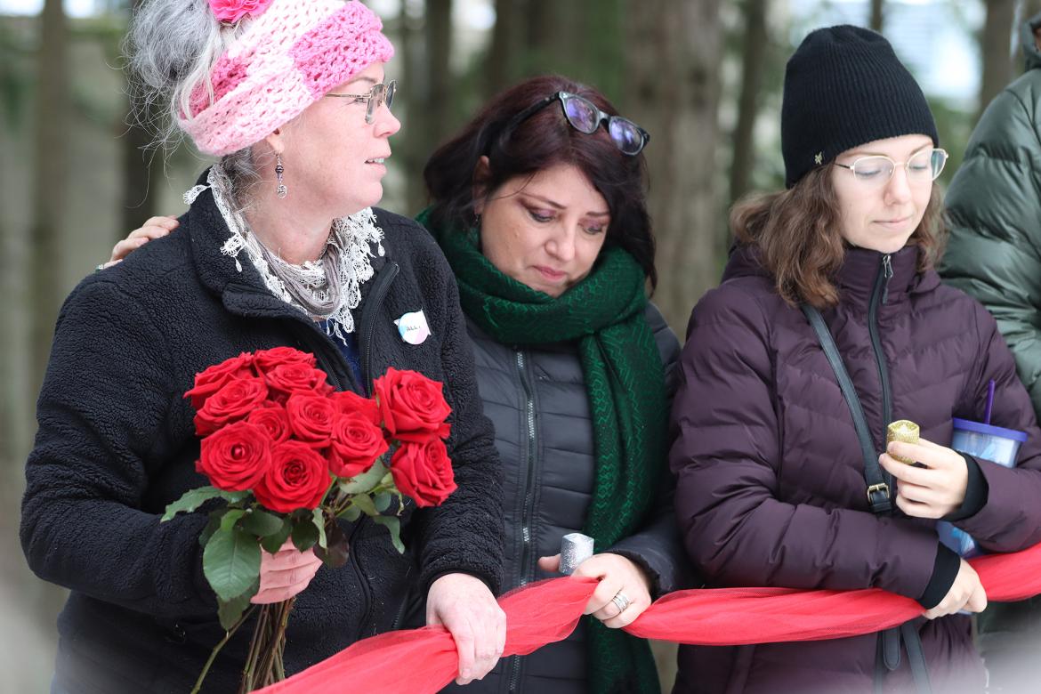 Eliza Gardiner holds a bouquet of red roses and stands next to Joy Gugeler and a student during the 2022 vigil.