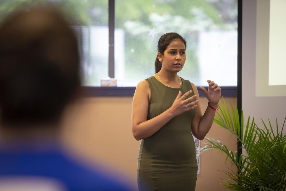 A student wearing a green dress stands in front of audience members and discusses their research during the 2019 CREATE Conference.
