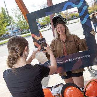 A student poses in a frame while another takes their photo