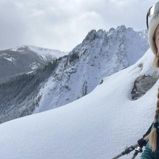 Andrea wearing ski gear smiles with a snowy mountainscape behind her