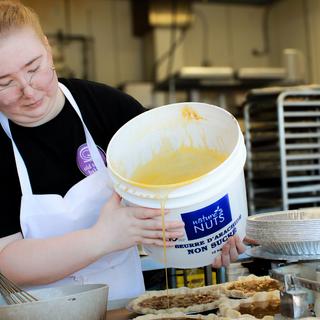 Faithe Haley, wearing a black shirt and white apron, pours sugar into pies in an industrial kitchen.