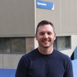 Jordan Herbison standing outside the VIU gym in a sunny day and smiling.