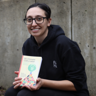Lauren Touchant sitting outside and displaying her book and smiling at the camera.
