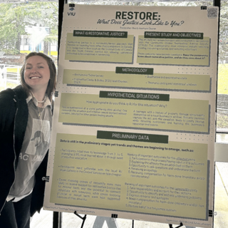 Madelyn Reetham-Clayton  standing beside her research poster and smiling.