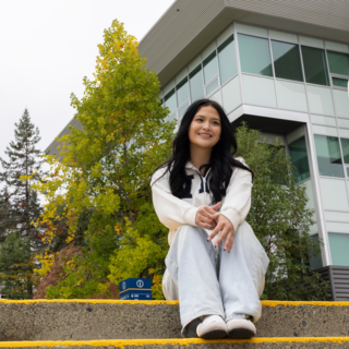 Marissa Tom-Charlie sitting on steps outside on a cloudy day, smiling and looking off into the distance
