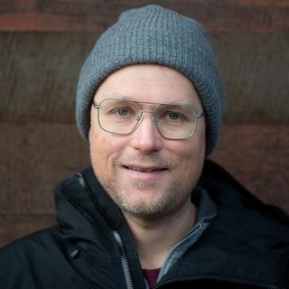 a headshot of trevor wideman, who is wearing a jacket, toque and glasses